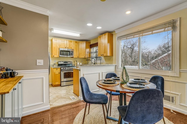 kitchen with crown molding, light stone counters, appliances with stainless steel finishes, kitchen peninsula, and light hardwood / wood-style floors