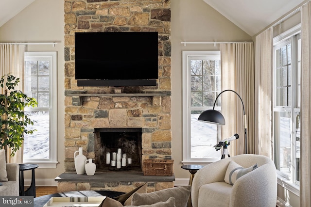 living room featuring hardwood / wood-style floors, vaulted ceiling, a stone fireplace, and a wealth of natural light