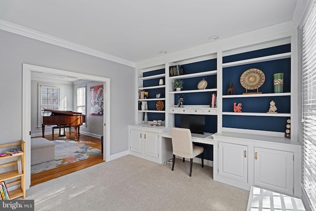 carpeted home office with crown molding, built in desk, and built in shelves