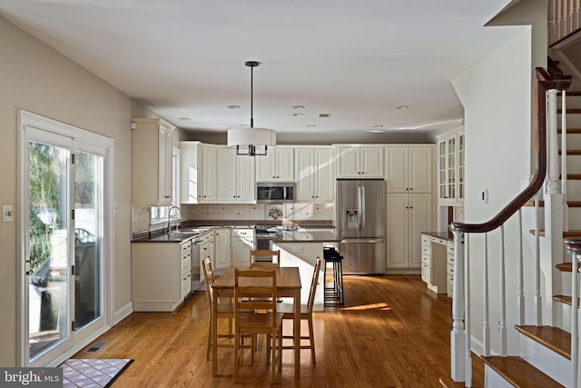 kitchen featuring sink, tasteful backsplash, hanging light fixtures, stainless steel appliances, and light hardwood / wood-style floors