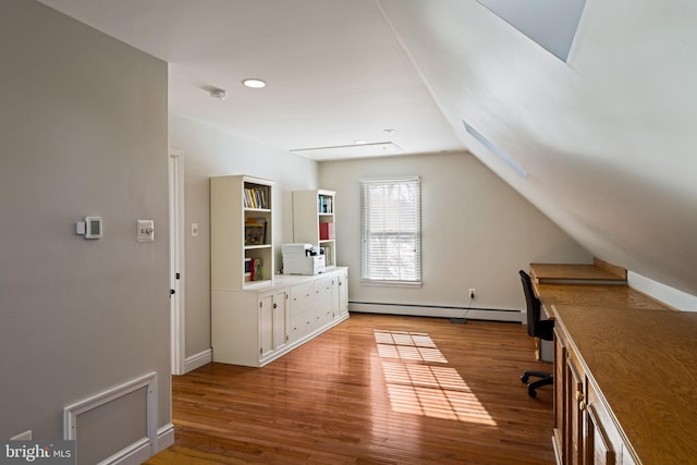 unfurnished office featuring lofted ceiling, a baseboard heating unit, and light wood-type flooring