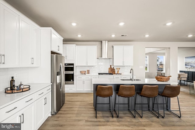 kitchen with sink, stainless steel fridge, white cabinets, and wall chimney exhaust hood