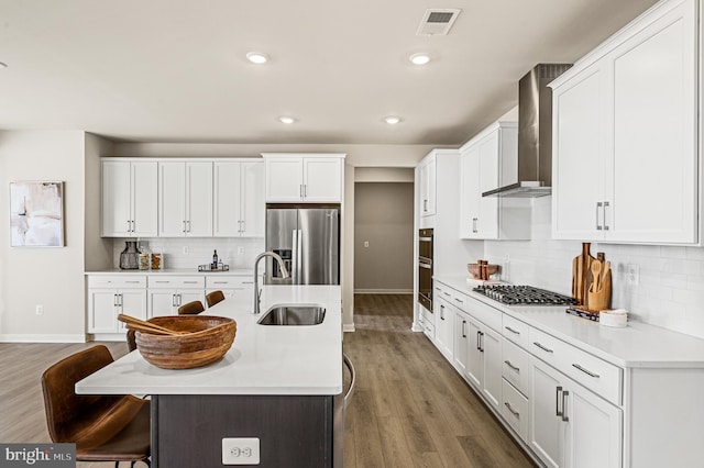 kitchen featuring wall chimney exhaust hood, stainless steel appliances, white cabinetry, a kitchen breakfast bar, and sink