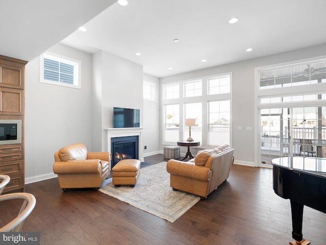 living room with dark wood-style floors, a glass covered fireplace, and baseboards