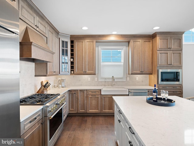 kitchen featuring custom range hood, glass insert cabinets, appliances with stainless steel finishes, dark wood-style flooring, and a sink