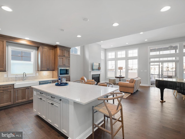 kitchen featuring a sink, white cabinetry, open floor plan, a center island, and stainless steel microwave