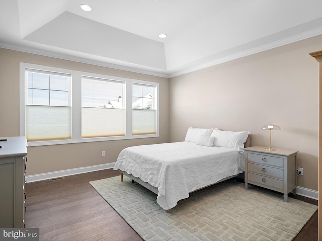 bedroom with crown molding, wood finished floors, a raised ceiling, and baseboards