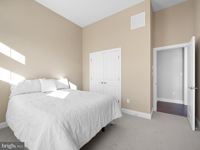 bedroom with a closet, visible vents, a high ceiling, light carpet, and baseboards