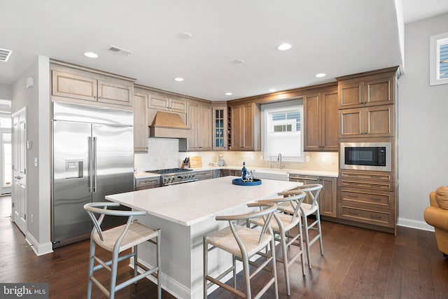 kitchen with a center island, built in appliances, custom range hood, a breakfast bar, and sink