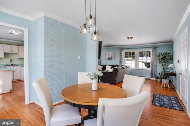 dining area with ornamental molding, light hardwood / wood-style flooring, and sink