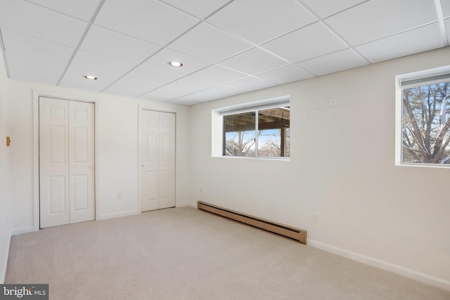 unfurnished bedroom featuring light carpet, multiple closets, a drop ceiling, and a baseboard radiator