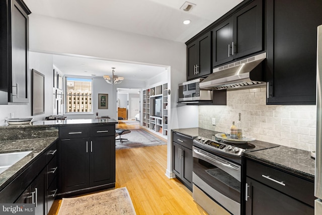 kitchen featuring appliances with stainless steel finishes, light wood-type flooring, dark stone countertops, backsplash, and an inviting chandelier