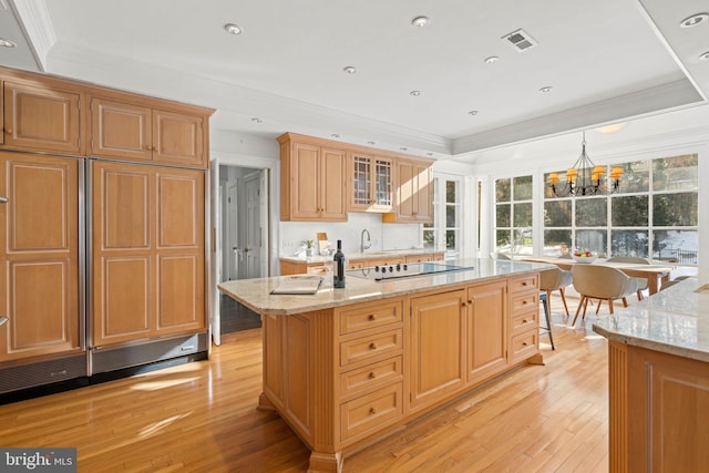 kitchen with light stone counters, a kitchen island with sink, decorative light fixtures, and a chandelier