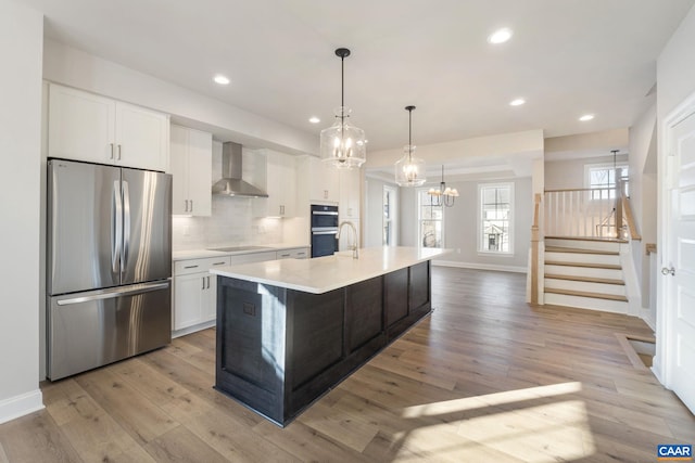 kitchen with white cabinetry, black appliances, an island with sink, decorative backsplash, and wall chimney exhaust hood