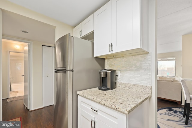 kitchen with dark wood-type flooring, stainless steel refrigerator, backsplash, light stone counters, and white cabinets