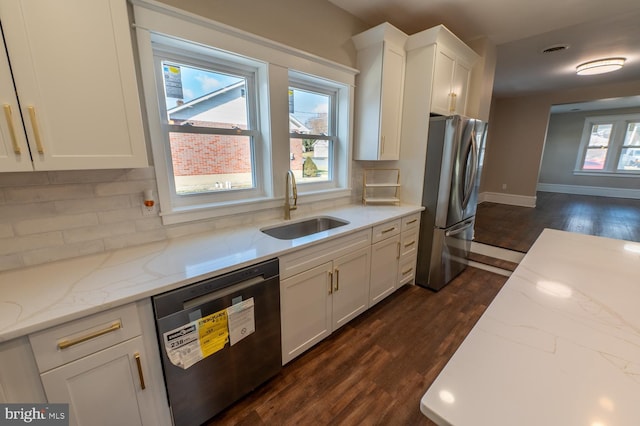 kitchen featuring light stone counters, dishwasher, stainless steel fridge, white cabinetry, and sink