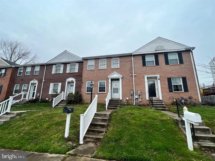 townhome / multi-family property featuring brick siding, entry steps, and a front lawn