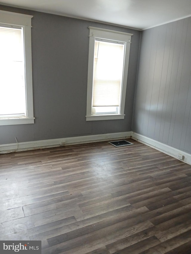 spare room featuring dark wood-type flooring, plenty of natural light, and wood walls