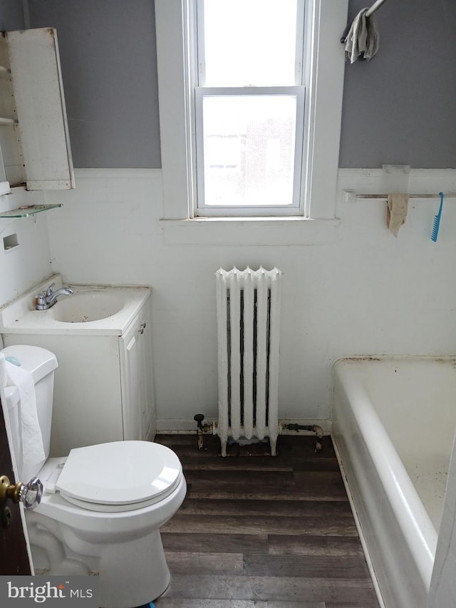 bathroom with radiator, hardwood / wood-style floors, a bathtub, vanity, and toilet