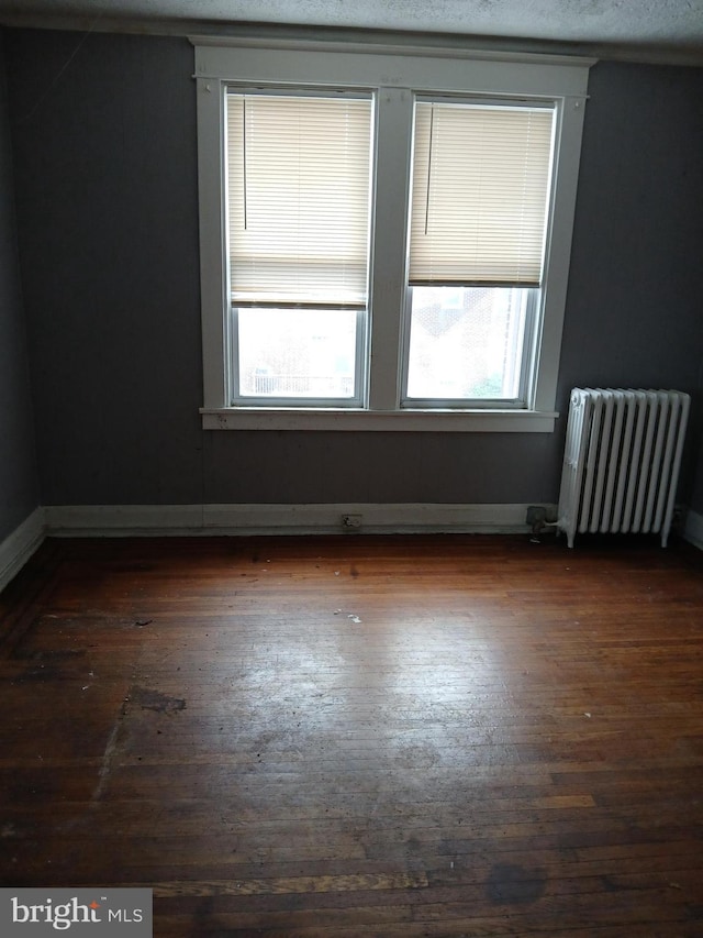 unfurnished room featuring radiator heating unit and dark hardwood / wood-style flooring