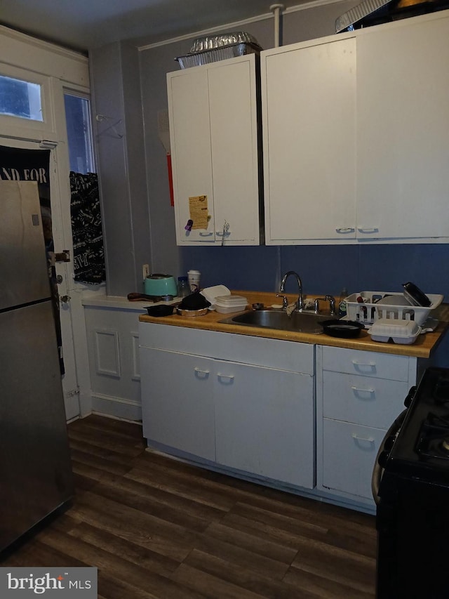 kitchen with black stove, sink, stainless steel refrigerator, dark hardwood / wood-style flooring, and white cabinets