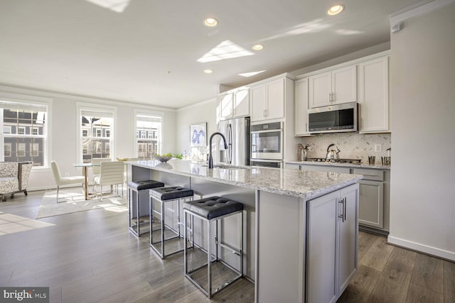 kitchen with appliances with stainless steel finishes, sink, a center island with sink, and wood-type flooring