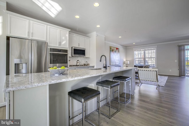 kitchen featuring sink, white cabinetry, a large island with sink, a breakfast bar area, and appliances with stainless steel finishes