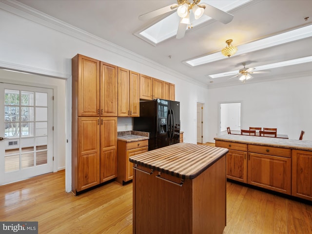 kitchen featuring a kitchen island, a skylight, black fridge, ornamental molding, and light wood-type flooring