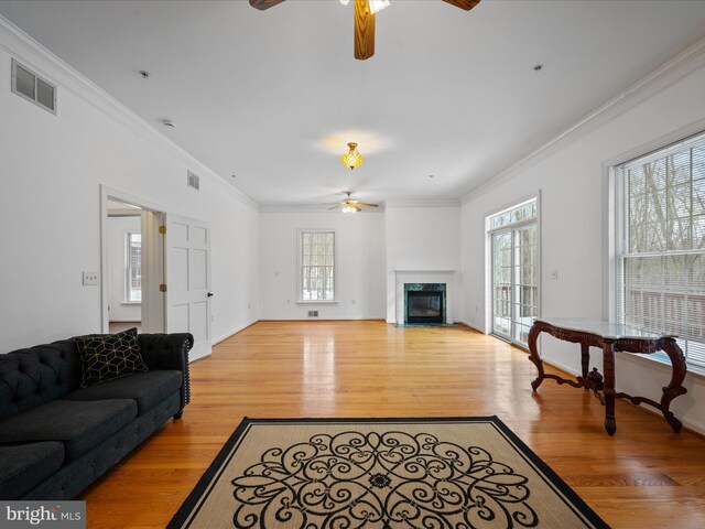 living room with ceiling fan, a high end fireplace, crown molding, and light wood-type flooring