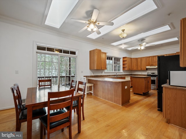 kitchen featuring a skylight, ceiling fan, stainless steel stove, crown molding, and a center island