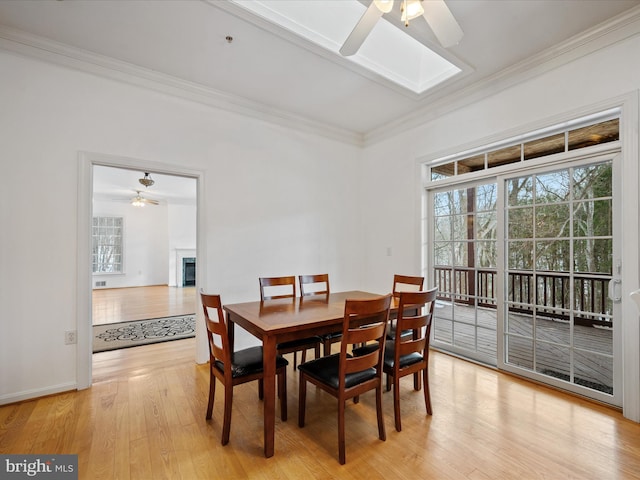 dining area featuring light wood-type flooring, ceiling fan, a skylight, and ornamental molding