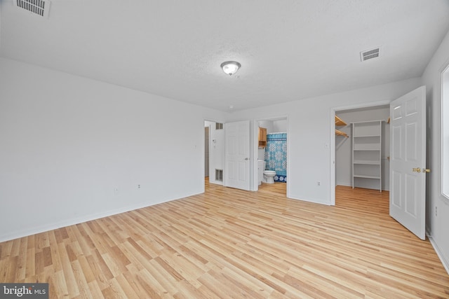 unfurnished bedroom with connected bathroom, a walk in closet, light hardwood / wood-style floors, a textured ceiling, and a closet