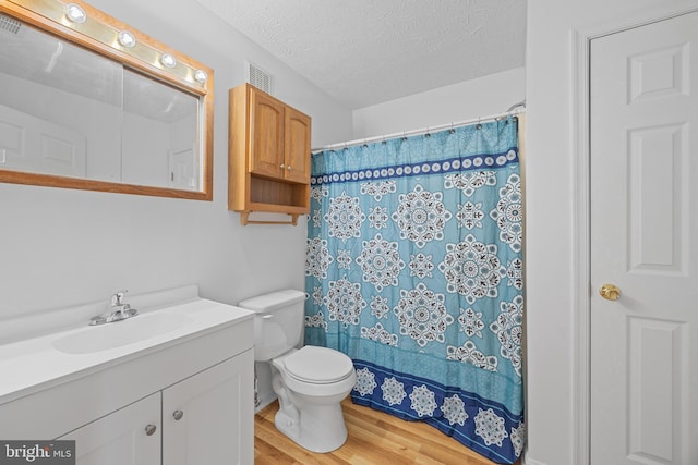 bathroom featuring hardwood / wood-style floors, vanity, walk in shower, toilet, and a textured ceiling