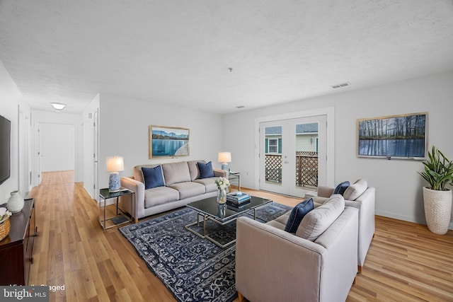 living room with french doors, a textured ceiling, and light wood-type flooring