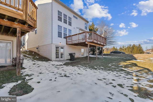 snow covered rear of property with a wooden deck and french doors