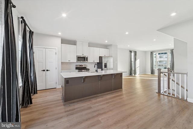 kitchen featuring stainless steel appliances, a large island, white cabinets, light wood-type flooring, and decorative backsplash