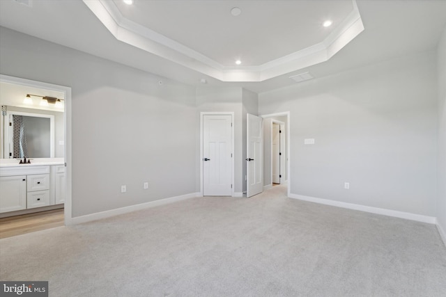 unfurnished bedroom featuring sink, a raised ceiling, light carpet, connected bathroom, and crown molding