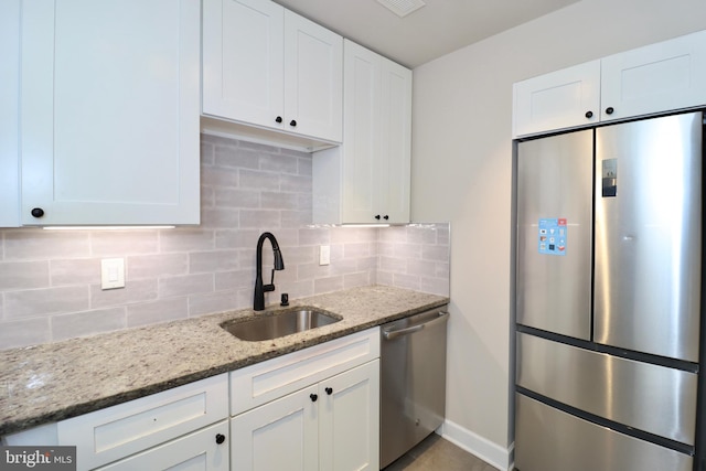 kitchen featuring appliances with stainless steel finishes, light stone countertops, sink, white cabinetry, and backsplash