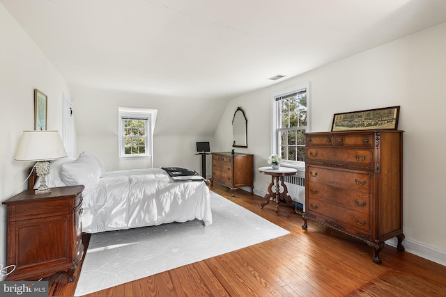 bedroom with multiple windows, lofted ceiling, and wood-type flooring