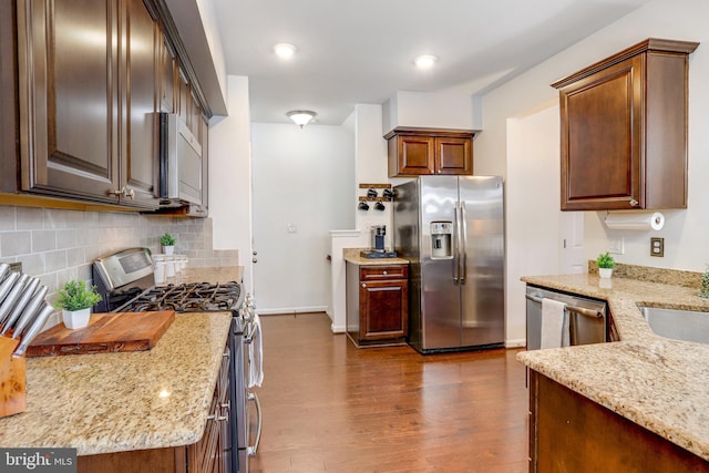 kitchen with appliances with stainless steel finishes, dark hardwood / wood-style flooring, light stone counters, and decorative backsplash