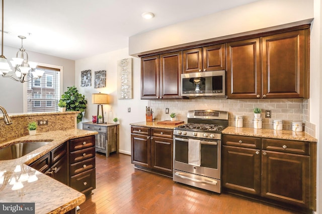 kitchen with appliances with stainless steel finishes, dark brown cabinetry, sink, an inviting chandelier, and decorative light fixtures