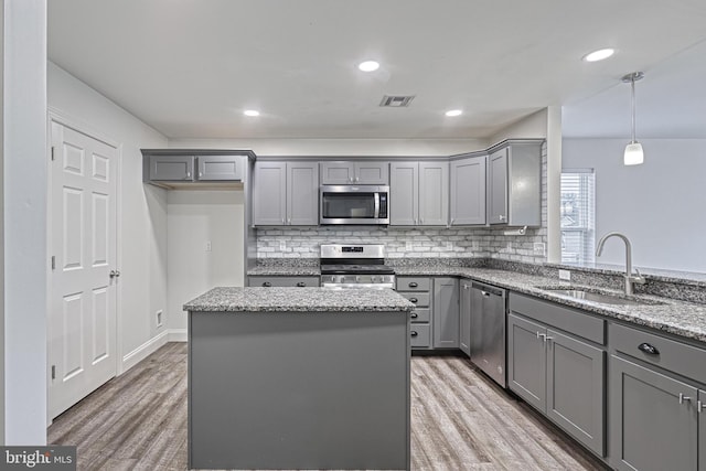 kitchen featuring gray cabinets, appliances with stainless steel finishes, decorative light fixtures, sink, and a center island