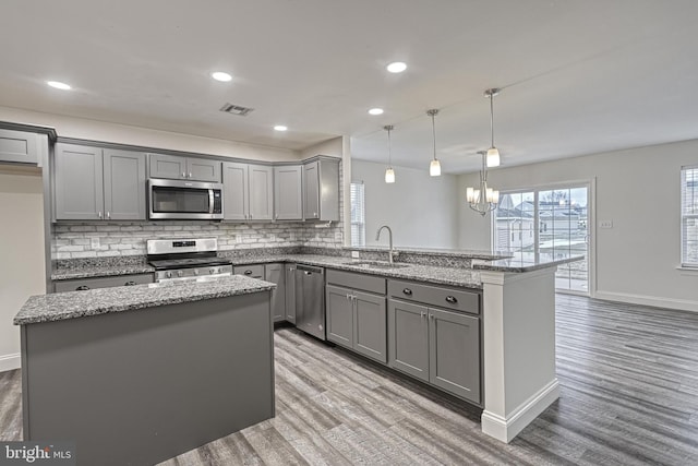 kitchen featuring gray cabinets, a kitchen island, sink, hanging light fixtures, and appliances with stainless steel finishes