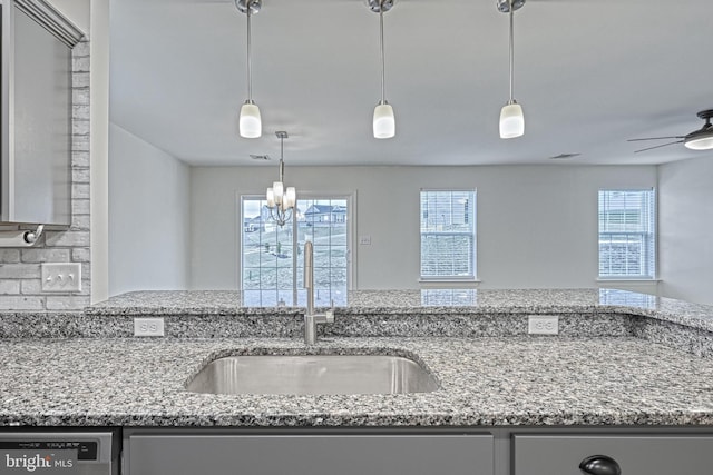 kitchen featuring ceiling fan with notable chandelier, stainless steel dishwasher, light stone counters, and sink