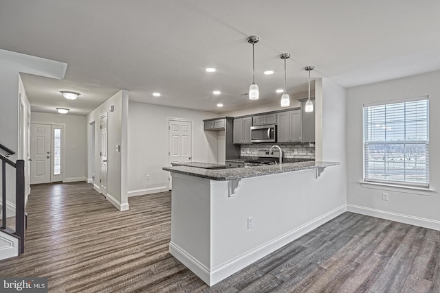 kitchen featuring pendant lighting, dark hardwood / wood-style flooring, stainless steel appliances, gray cabinets, and kitchen peninsula