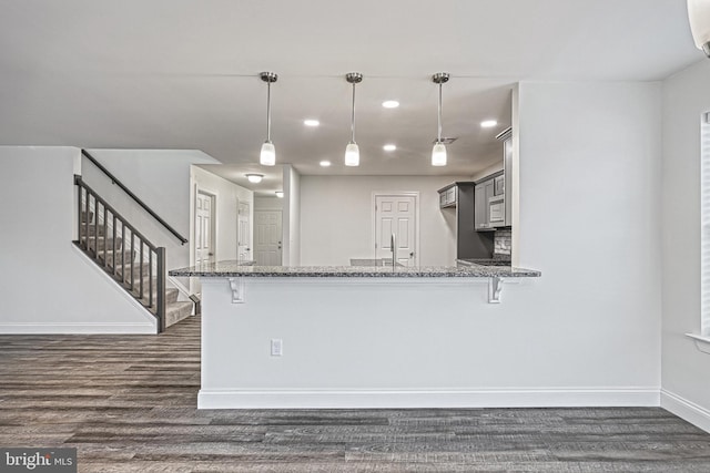 kitchen featuring pendant lighting, kitchen peninsula, dark wood-type flooring, a kitchen breakfast bar, and light stone counters