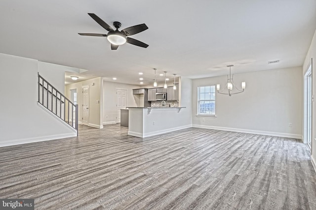 unfurnished living room with ceiling fan with notable chandelier and hardwood / wood-style floors