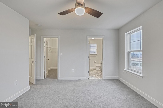 unfurnished bedroom featuring a spacious closet, light carpet, ensuite bathroom, ceiling fan, and a closet