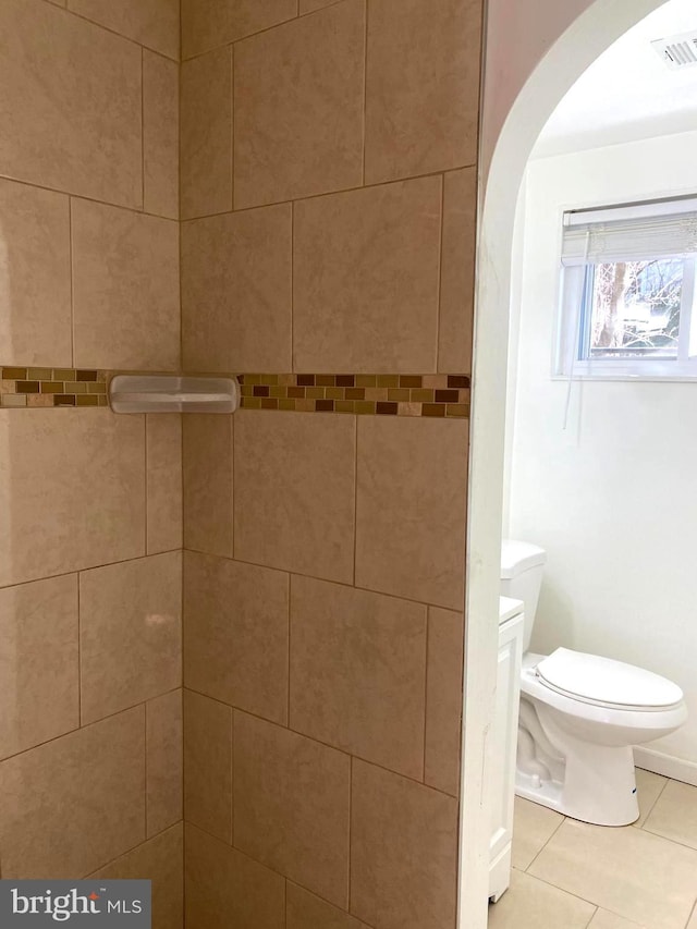 bathroom featuring toilet, tile patterned flooring, and a tile shower