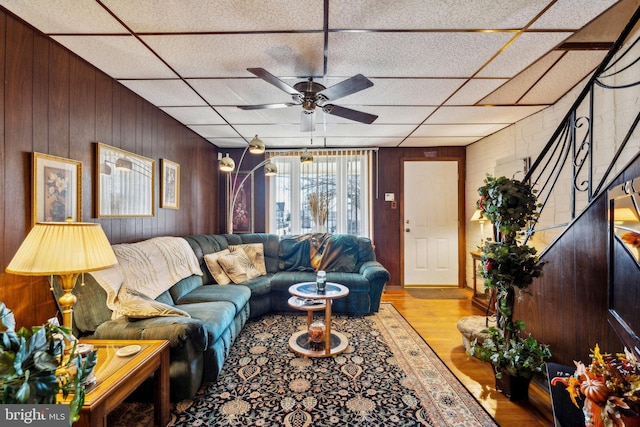 living room featuring a drop ceiling, wooden walls, and ceiling fan